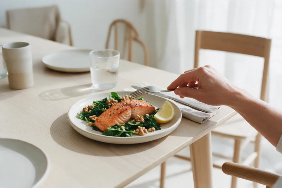 A plate of grilled salmon with greens, lemon and walnuts on a wooden table