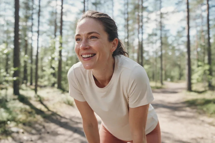 A woman smiling as she catches her breath after a run on a forest trail