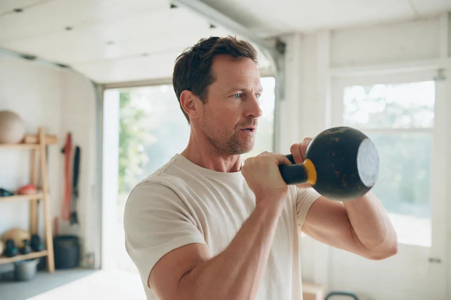 A man lifting a kettlebell in a bright home gym